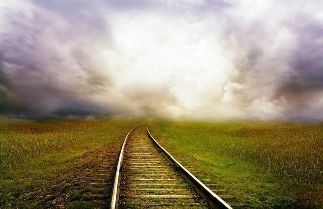 railroad-track-in-fields-under-cloudy-sky